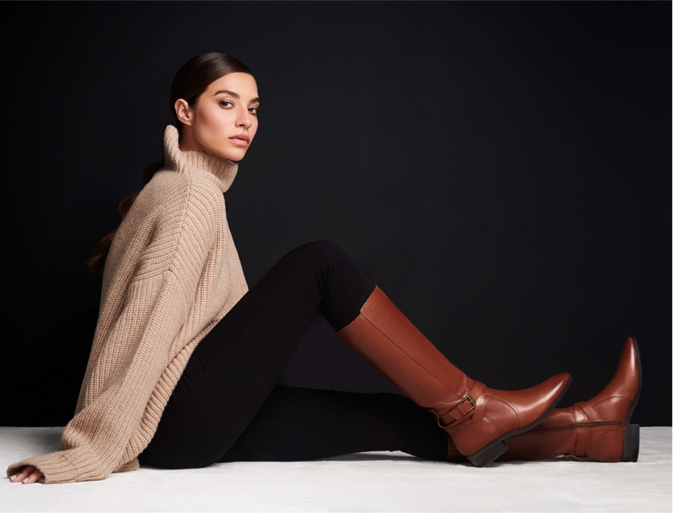 a woman sitting on the ground with one leg outstretched wearing a pair of brown knee high riding boots